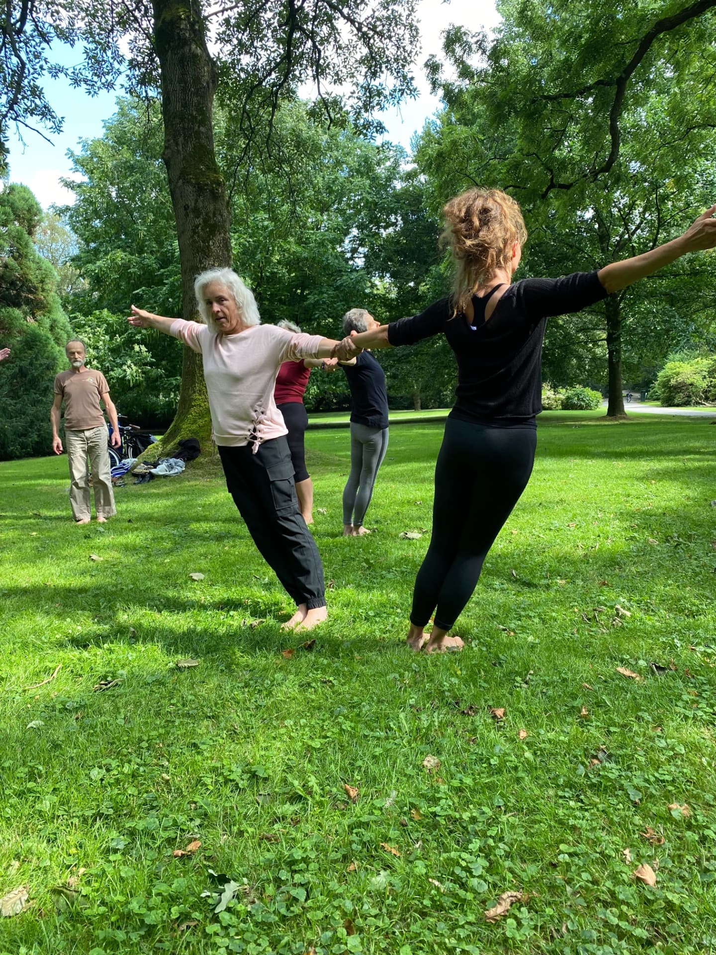 Deelnemers met gespreide armen tijdens een buitenles in het park