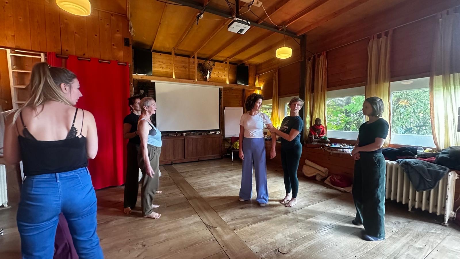 Deelnemers staan in een kring in een houten zaal tijdens de workshop in Creil